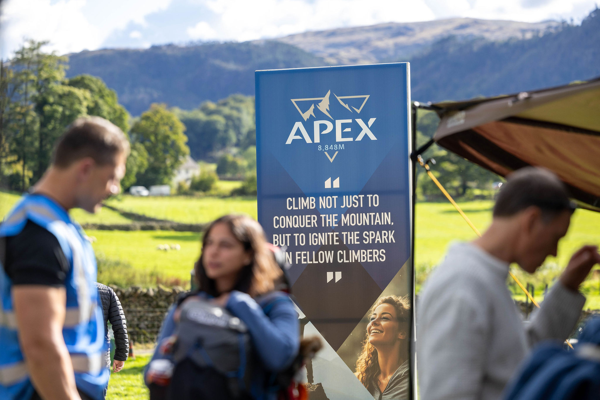 people talking in front of an APEX everest banner. helvellyn in background.